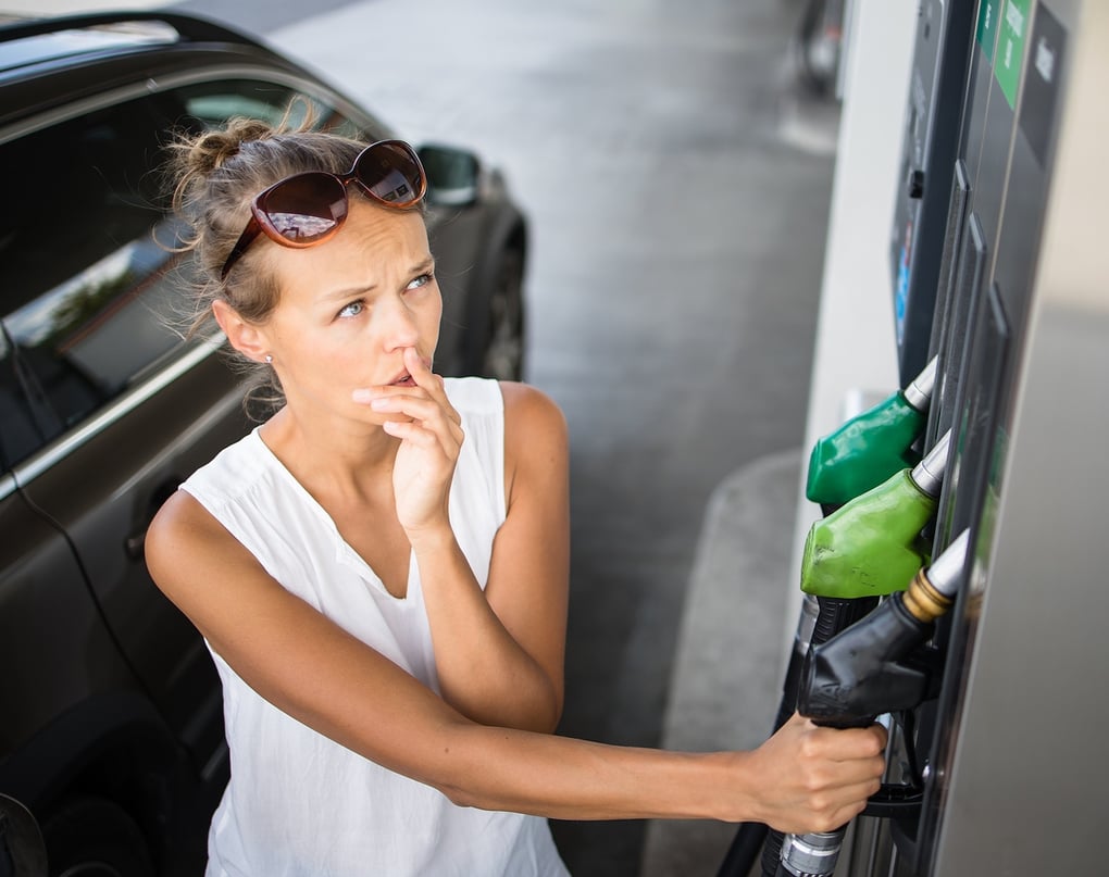woman at gas station looking upset at prices